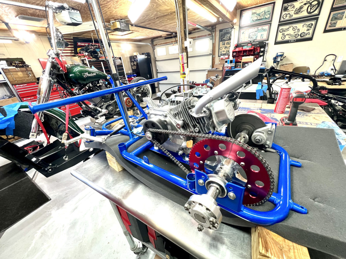 DKCC Bar-Hag — frame and engine assembly on workbench showing red sprocket, chain drive and rear axle